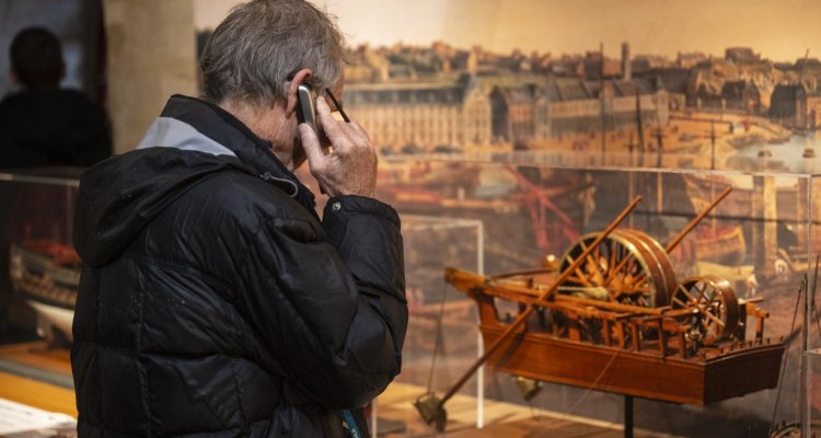 Visiteur avec un audioguide devant un modèle de bateau